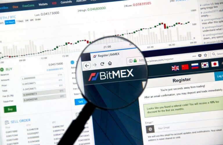 Uma tela de computador exibe o site da BitMEX com uma página de cadastro aberta. Uma lupa destaca a aba do navegador mostrando o logo da BitMEX. Ao fundo, gráficos de trading e tabelas de dados detalham insights sobre as taxas da BitMEX e seu impacto nas decisões dos traders.  